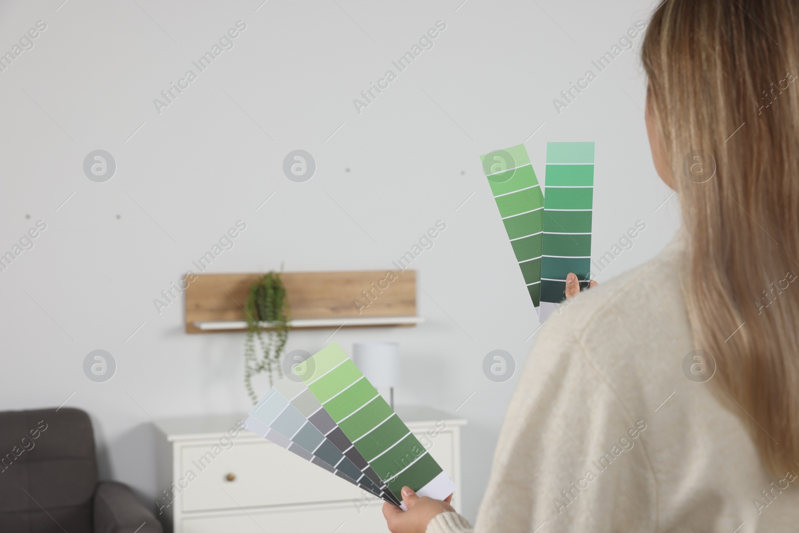 Photo of Woman choosing color for wall in room, focus on hands with paint chips. Interior design