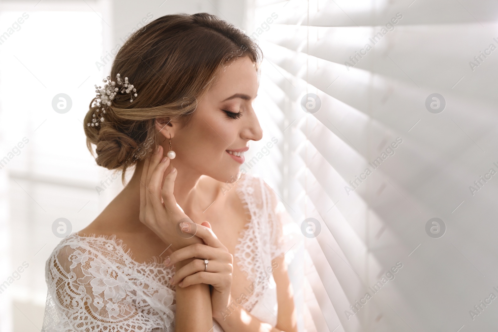 Photo of Young bride with elegant wedding hairstyle near window indoors