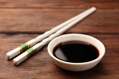 Bowl with soy sauce and chopsticks on wooden table, closeup