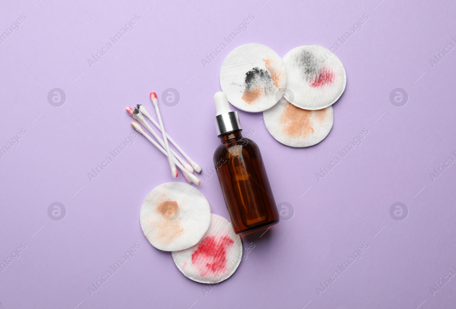 Photo of Dirty cotton pads, swabs and makeup removal product on violet background, flat lay