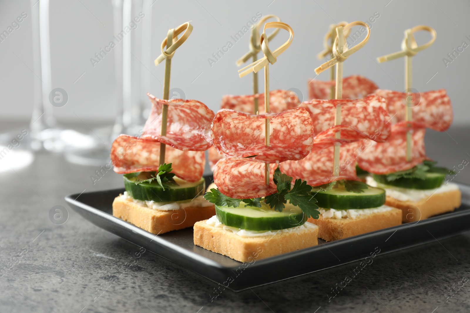 Photo of Tasty canapes with salami, cucumber and cream cheese on grey table, closeup