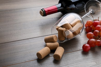 Photo of Bottle of wine, glass with corks and grapes on wooden table