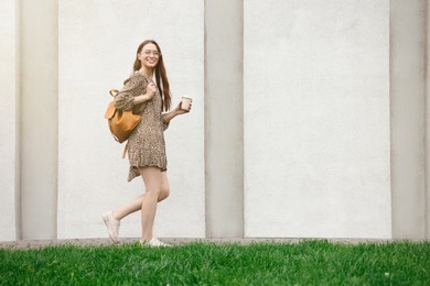 Photo of Young woman with cup of drink walking near stone wall outdoors, space for text