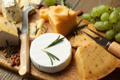 Photo of Cheese platter with specialized knife and fork on wooden table, closeup