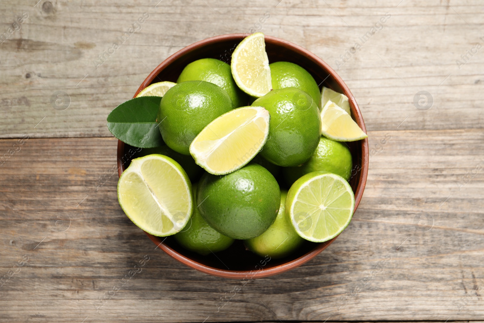 Photo of Tasty ripe limes in bowl on wooden table, top view