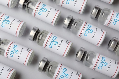 Photo of Glass vials with COVID-19 vaccine on light background, flat lay