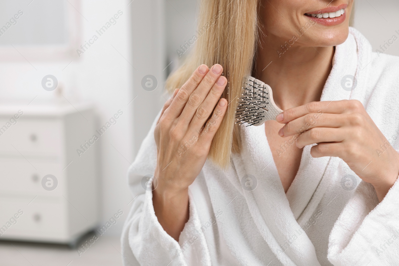 Photo of Woman in robe brushing her hair indoors, closeup