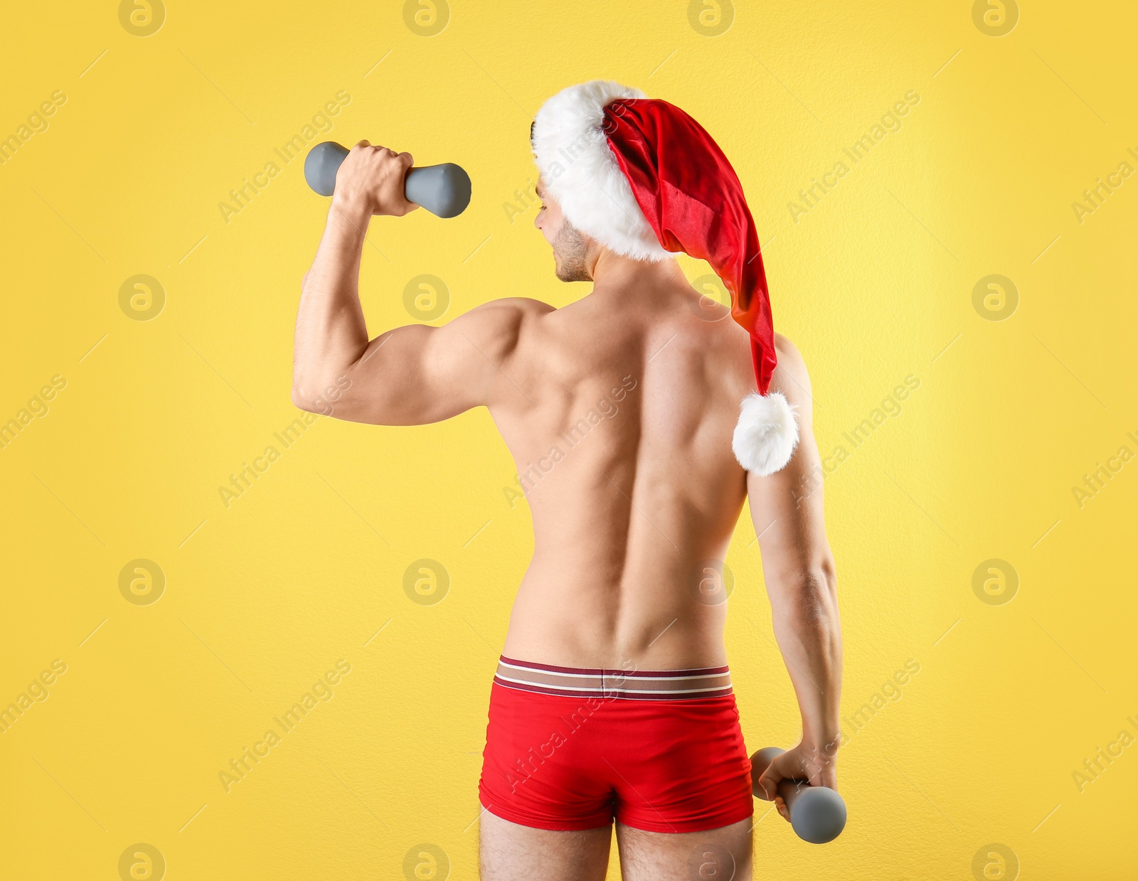 Photo of Shirtless sexy young Santa Claus with dumbbells on color background