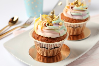 Photo of Plate with cute sweet unicorn cupcakes on white table, closeup