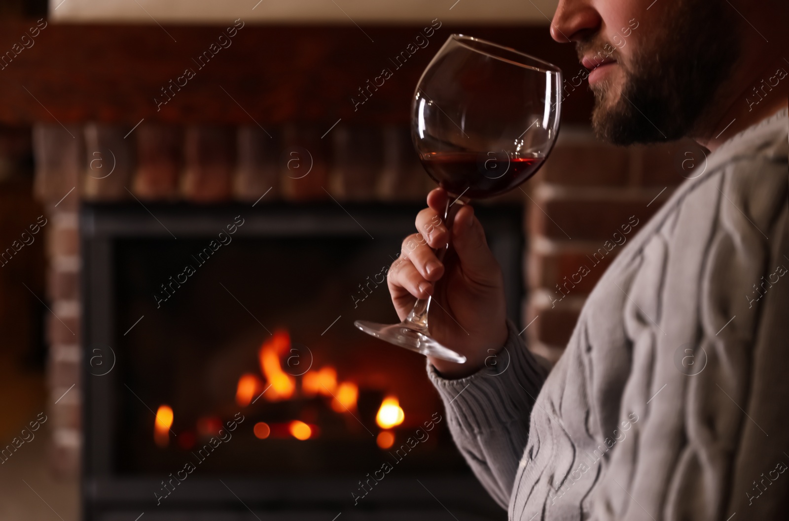 Photo of Man with glass of wine near fireplace at home, closeup