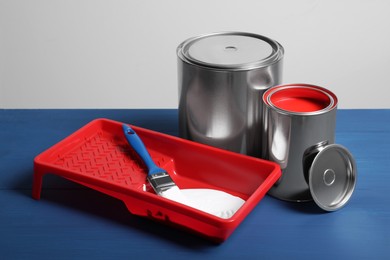 Photo of Cans of paints, brush and tray on blue wooden table