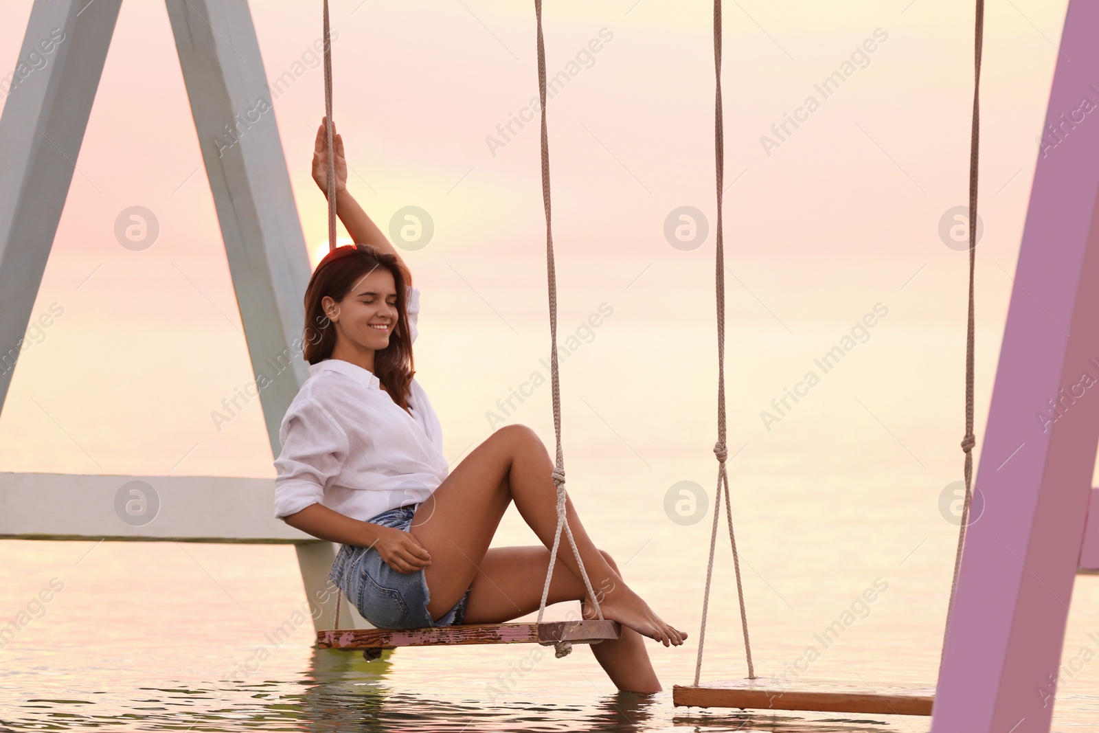 Photo of Young woman enjoying sunrise on swing over water