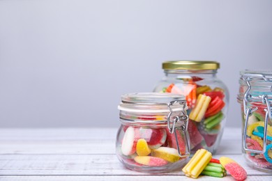 Tasty jelly candies in different jars on white wooden table, space for text