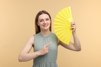 Happy woman with yellow hand fan pointing on beige background