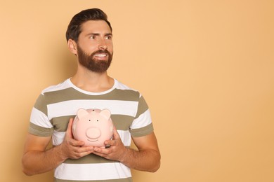 Happy man with ceramic piggy bank on beige background, space for text