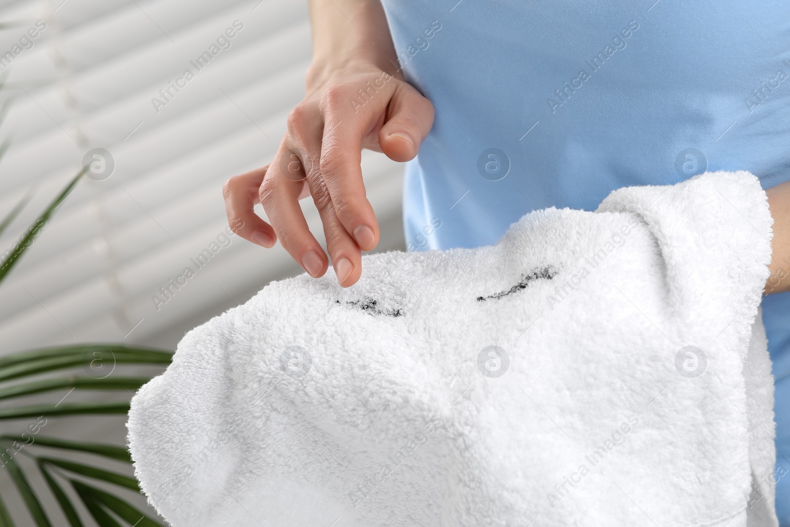 Photo of Woman holding terry towel with mascara spot indoors, closeup. Makeup removal