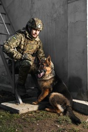 Photo of Ukrainian soldier with German shepherd dog sitting outdoors