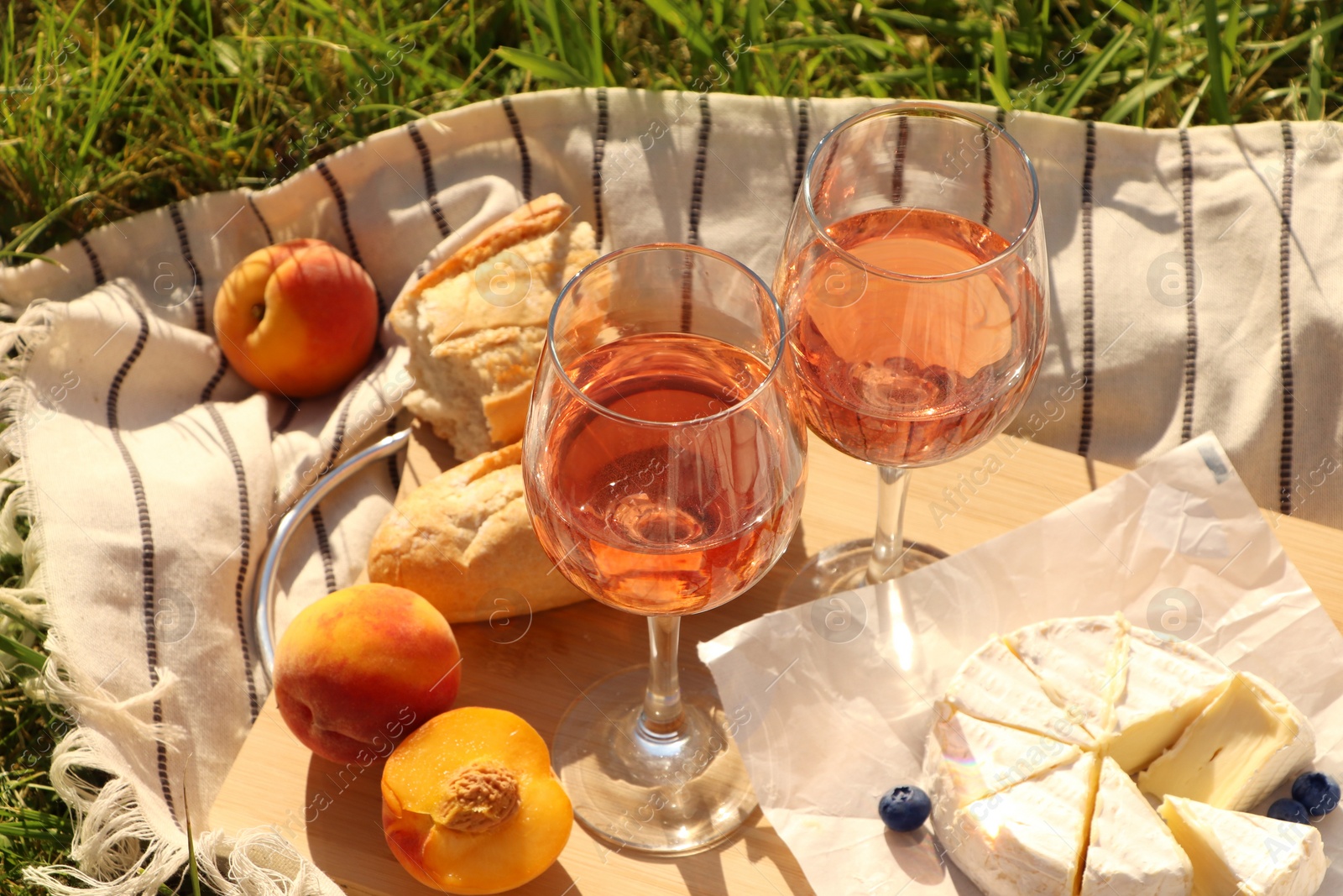 Photo of Glasses of delicious rose wine and food on picnic blanket outdoors