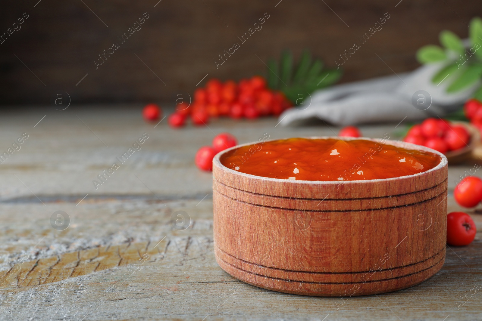 Photo of Delicious rowan jam in wooden bowl on table. Space for text