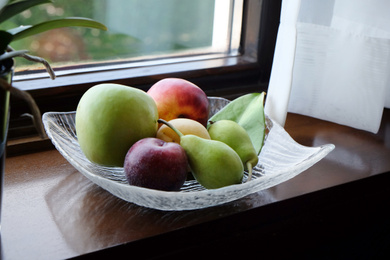 Juicy ripe fruits in vase on wooden window sill