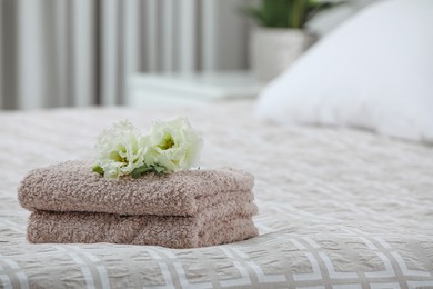 Stack of clean towels and Eustoma flowers on bed indoors, space for text
