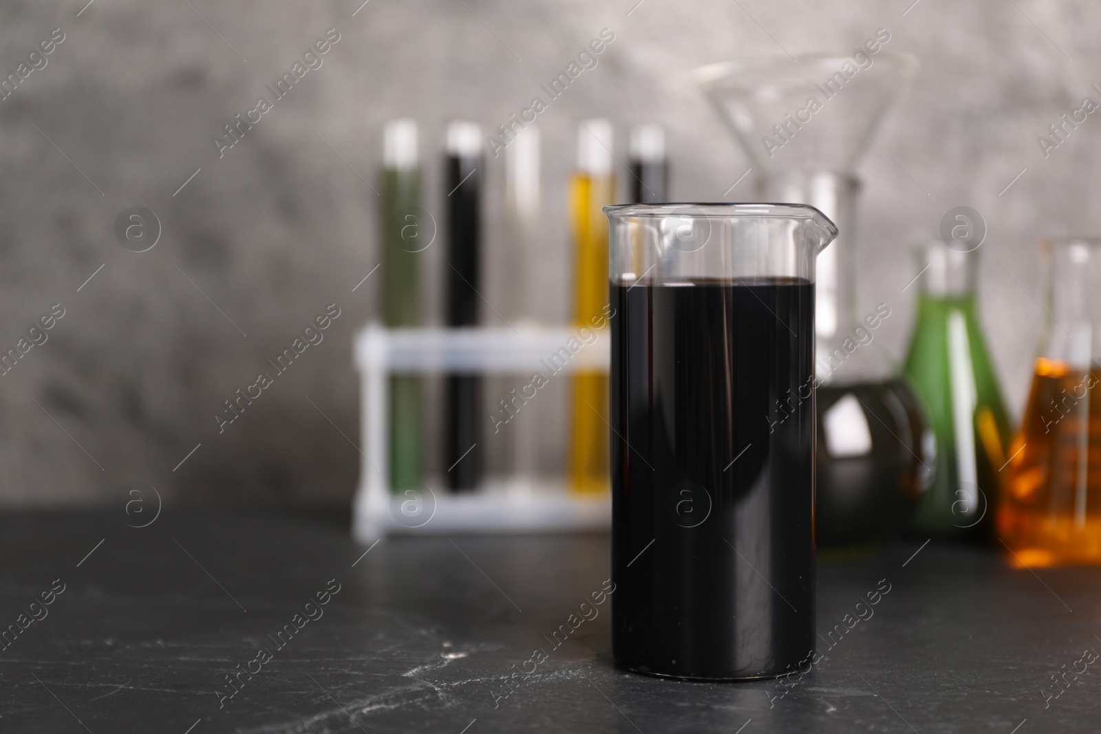 Photo of Beaker, flasks and test tubes with different types of oil on grey textured table, closeup. Space for text