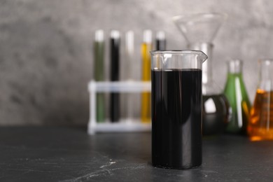 Beaker, flasks and test tubes with different types of oil on grey textured table, closeup. Space for text