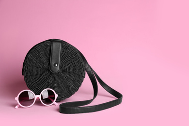 Stylish woman's bag and sunglasses on light pink background. Space for text