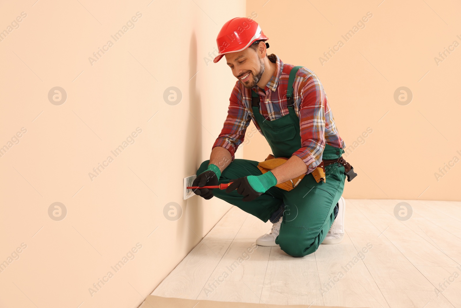 Photo of Electrician in uniform with screwdriver repairing power socket indoors