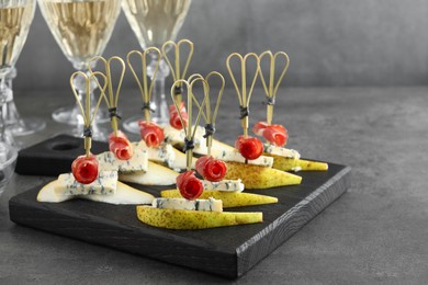 Photo of Tasty canapes with pears, blue cheese and prosciutto on grey table, closeup. Space for text
