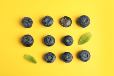 Tasty ripe blueberries and leaves on yellow background, flat lay