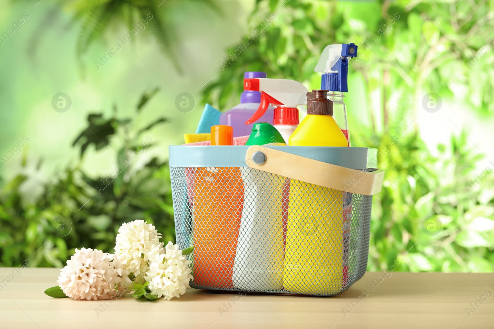 Photo of Spring flowers and basket with cleaning supplies on wooden table