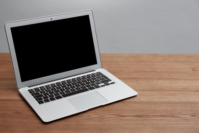 Modern laptop with blank screen on wooden table against gray background