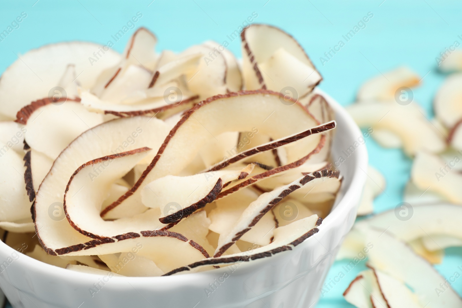 Photo of Tasty coconut chips in bowl on table, closeup