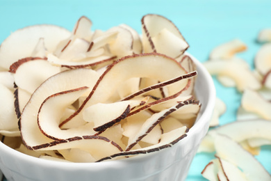 Tasty coconut chips in bowl on table, closeup