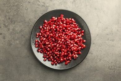 Photo of Ripe juicy pomegranate grains on grey textured table, top view