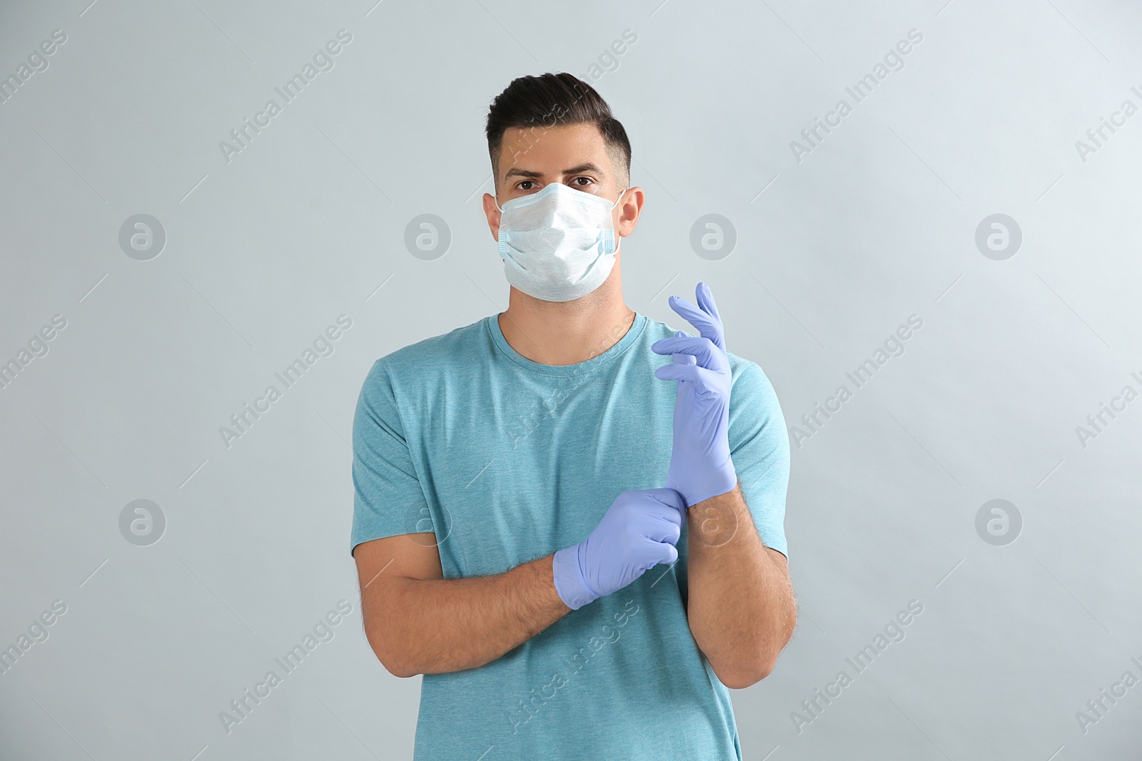 Photo of Man in protective face mask putting on medical gloves against grey background