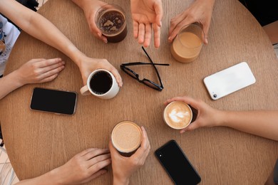 Friends drinking coffee at wooden table in cafe, top view