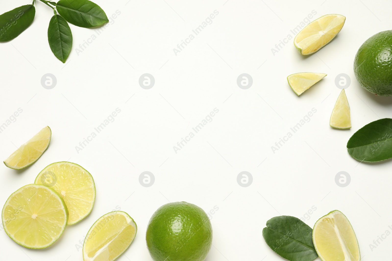 Photo of Whole and cut fresh ripe limes with green leaves on white background, flat lay