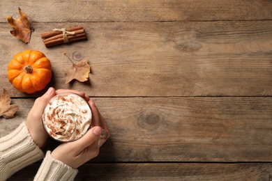 Photo of Woman holding tasty pumpkin latte at wooden table, top view. Space for text