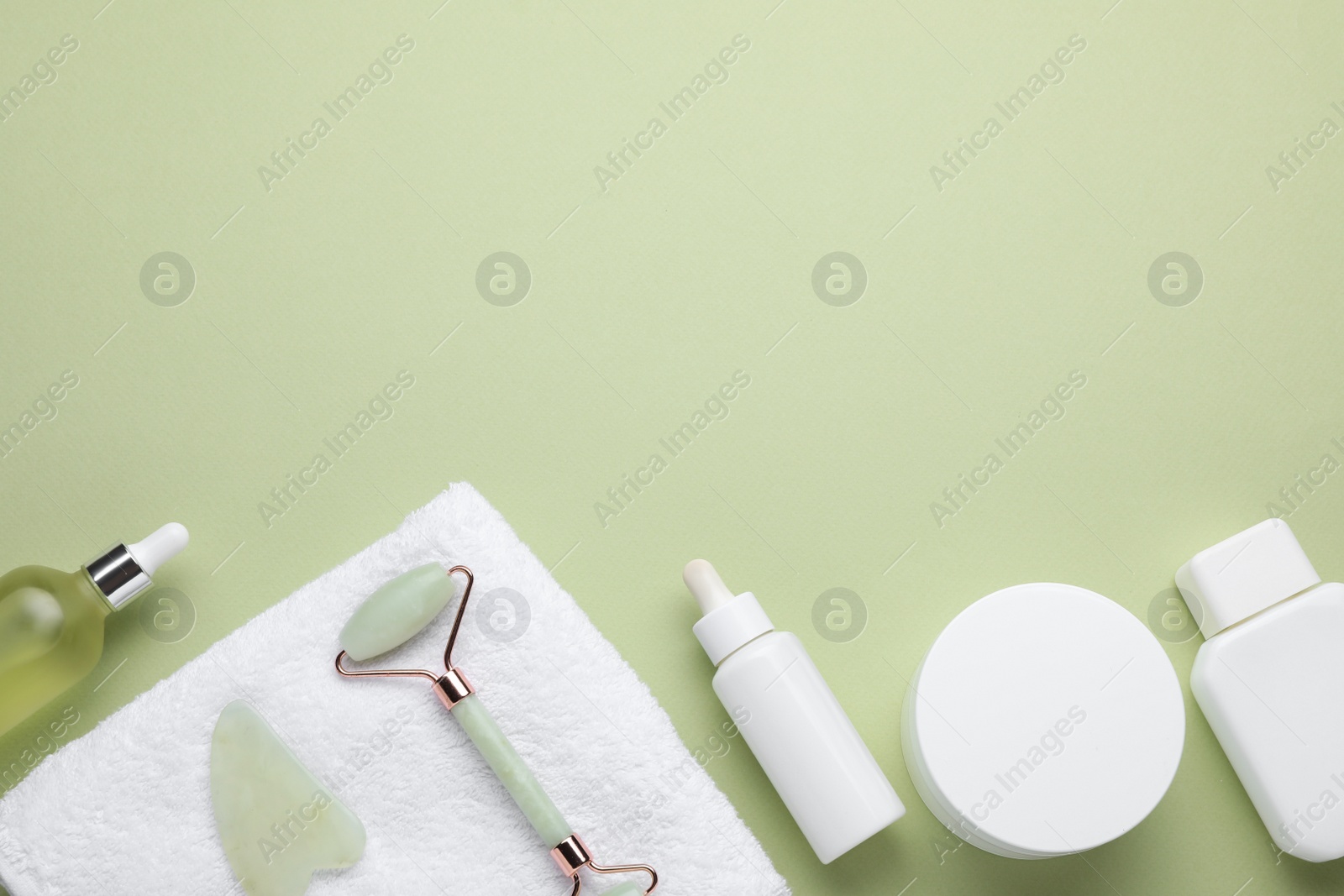 Photo of Natural face roller, gua sha tool, cosmetic products and towel on light green background, flat lay. Space for text