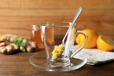 Photo of Spoon of grated ginger in glass cup and ingredients on wooden table