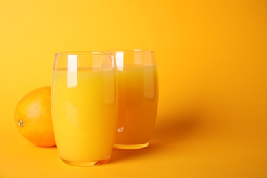 Photo of Freshly made orange juice in glasses on color background, space for text