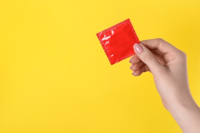 Woman holding condom on yellow background, closeup. Space for text