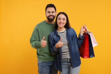 Photo of Happy couple with shopping bags showing thumbs up on orange background