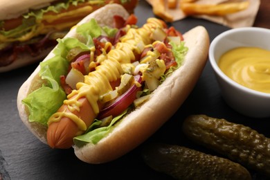 Delicious hot dog with lettuce, onion and pickle on table, closeup