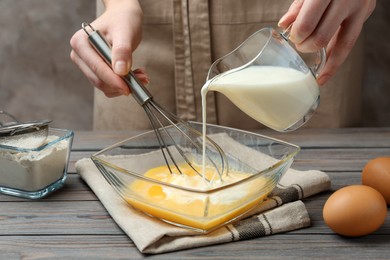 Photo of Woman adding milk to whisked eggs at wooden table, closeup