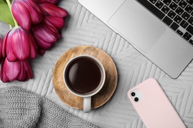 Beautiful tulips, cup of coffee, laptop, smartphone and sweater on light gray blanket, flat lay