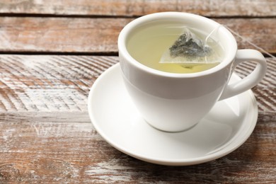 Photo of Tea bag in cup with hot drink on wooden rustic table, closeup. Space for text