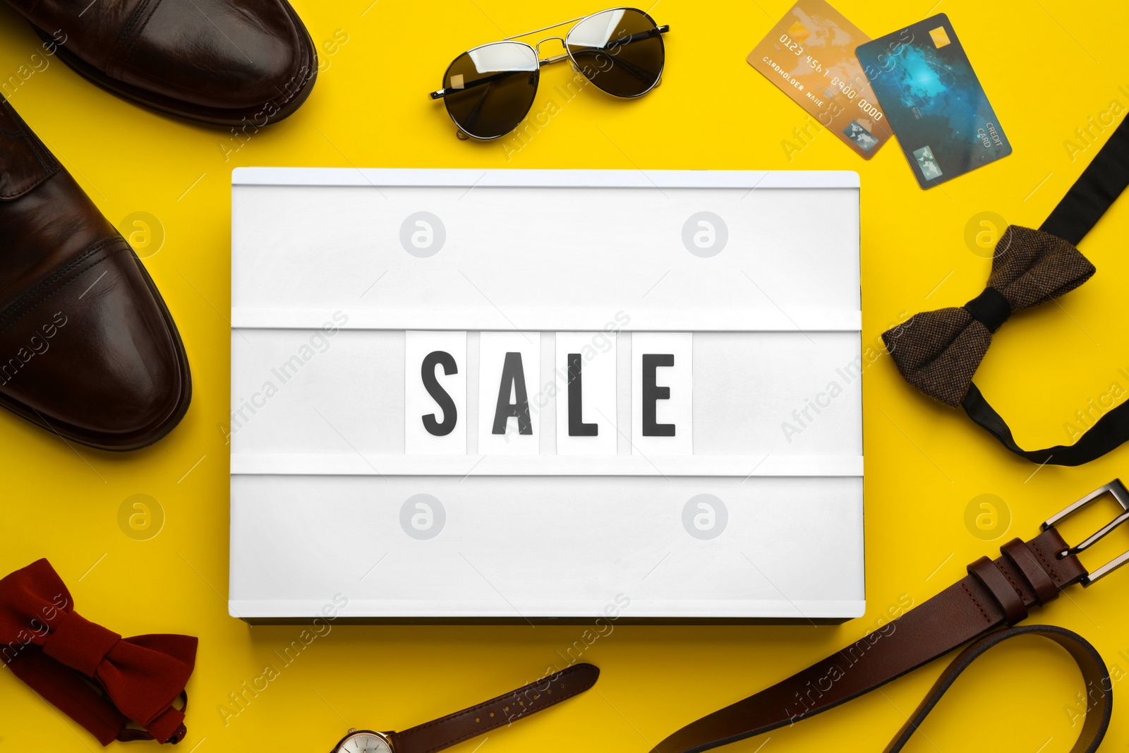 Photo of Light box with word Sale, men's accessories and credit cards on yellow background, flat lay